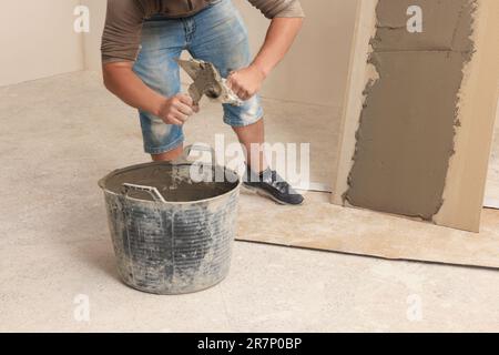 Worker applying adhesive mix on spatula near tile indoors, closeup Stock Photo