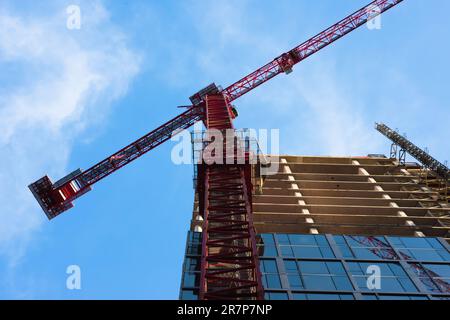 Majestic view of a red highrise crane operating against a bright blue sky. Shadows and reflections and striking perspective all add to the visual interest. Stock Photo