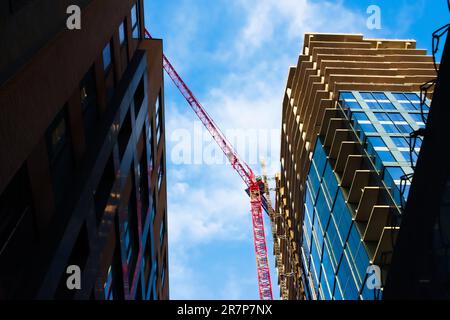 Majestic view of a red highrise crane operating against a bright blue sky. Shadows and reflections and striking perspective all add to the visual interest. Stock Photo