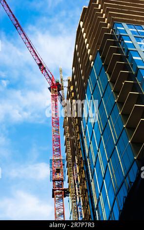 Majestic view of a red highrise crane operating against a bright blue sky. Shadows and reflections and striking perspective all add to the visual interest. Stock Photo