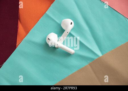 wireless white headphones lie on multi-colored fabrics, headset Stock Photo