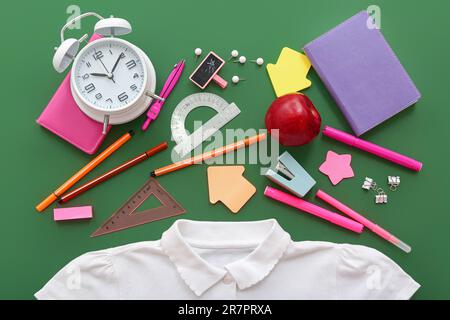 Stylish shirt with apple, alarm clock and different stationery on green background Stock Photo