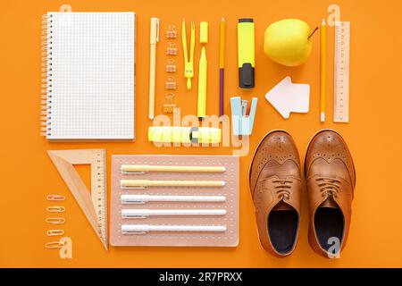 Cute shoes with fresh apple and different stationery on orange background Stock Photo