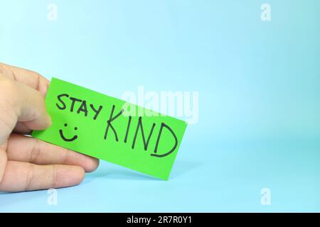Stay kind and kindness reminder concept. Hand holding a bright green paper message note. Stock Photo