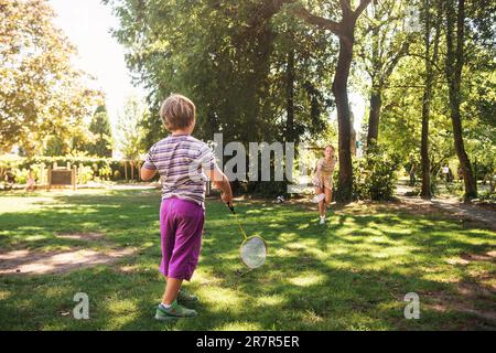 Group of 2 funny kids friends playing badminton in summer park. Children having fun together on a nice sunny day Stock Photo