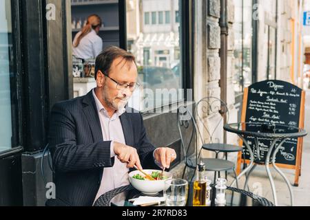 Businessman having lunch on a terrace in outdoor cafe, wearing a suit. Healthy green salad with salmon Stock Photo