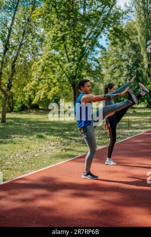 Young lovely couple stretching their legs, on a sports track in the park Stock Photo