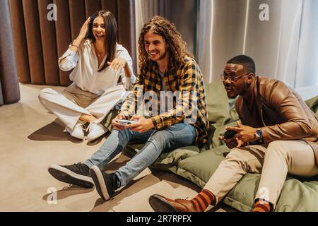 Beautiful, overjoyed multiracial colleagues having fun at work while taking a break. They are playing electronic games and smiling Stock Photo