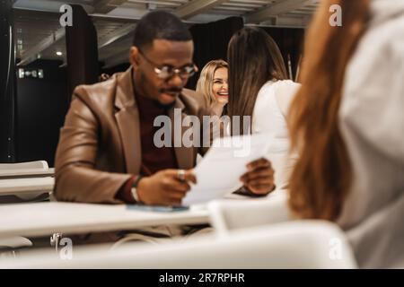 Two female employees having a conversation and laughing while their black male coworker is reading test questions Stock Photo