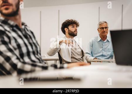 Handsome handicapped male junior employee in a wheelchair asking a questions while having a presentation at the classroom Stock Photo