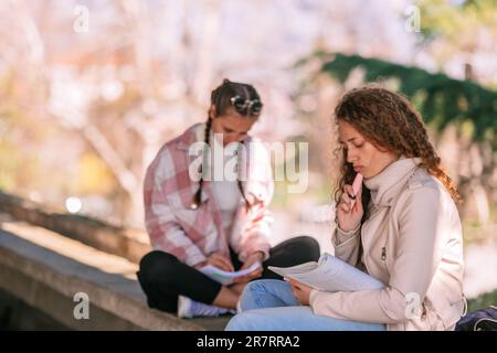 Lovely curly haired school girl reading book. She is trying to figure it out what that means. Brunette girl writing in notebook in the back Stock Photo