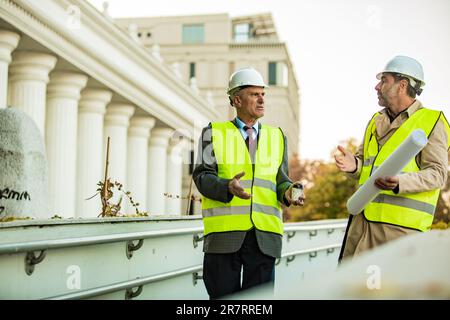 Two senior construction managers are standing and having a conversation about the new plans and ideas Stock Photo