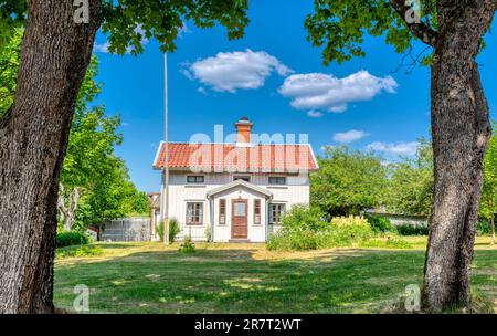 Traditional Swedish wooden house with red tiled roof surrounded by green trees under a bright blue summer sky, Sweden. Stock Photo