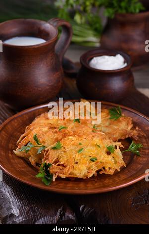 Potato fritters (a pancake, especially one made with grated potato) served with sour cream, herbs and a jug of milk. Country style. Stock Photo