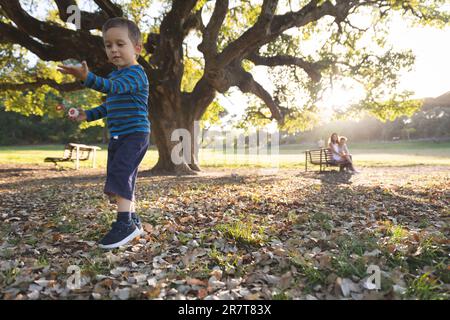A little boy playing with soap bubbles and his parents watching him in the distanse. Mid shot Stock Photo