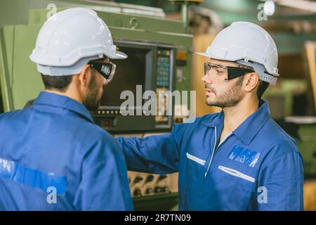 Engineer Worker Training Team Friend to operate using lathe milling CNC machine in heavy metal factory. Stock Photo