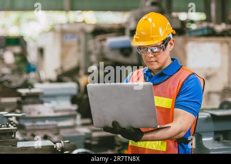 Asian male engineer worker happy using Laptop computer in heavy metal factory background. Stock Photo