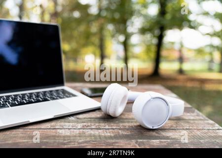 Laptop and headphones on a wooden table in the autumn park Stock Photo
