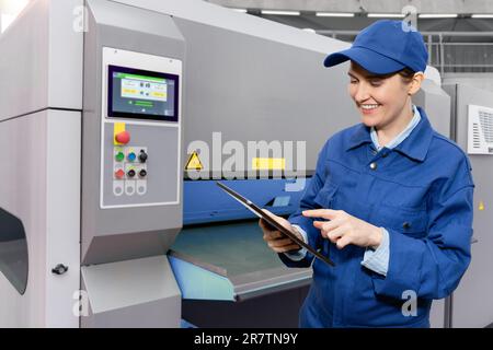 Woman worker with digital tablet controls automatic machine tool in smart factory. Stock Photo
