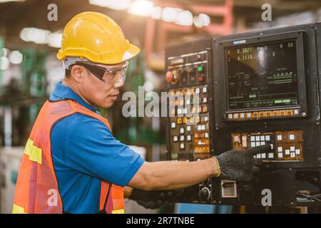 Industrial Asian worker operating lathe milling CNC machine at metal machining heavy industry. Stock Photo