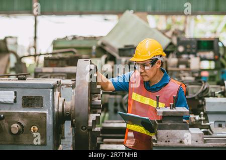 Young Asian Technician Engineer Staff Worker using Lathe CNC Milling Machine work in Heavy Metal Factory. Stock Photo