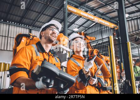 Engineer team working with robot welding in automation factory. People worker in safety suit control robotic arm in automated manufacturing industry t Stock Photo