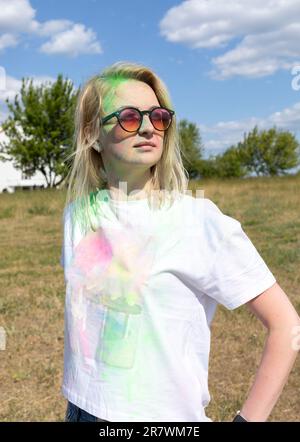 Portrait Pretty Blond Woman With Colored Dye, Powder On Face And Cloth On Holi Colors Festival In Meadow, Sunny Day. Playful Cultural Event With Stock Photo