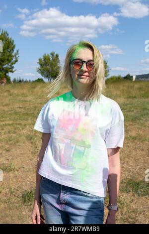 Smiling Beautiful White Blond Woman With Colorful Dye, Powder On Face, Cloth On Holi Colors Festival In Park, Sunny Day. Playful Cultural Event With Stock Photo