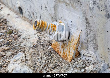 twisted metal nut covered with rust on the concrete wall of the bridge. Details of steel construction Stock Photo
