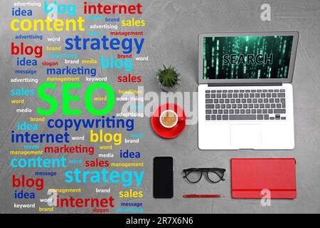 Search engine optimization (SEO). Marketing terms, laptop and stationery on grey textured table, flat lay Stock Photo