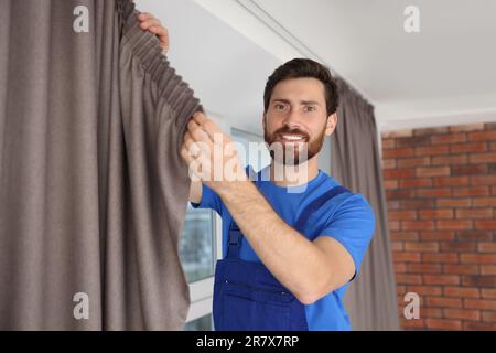 Worker in uniform hanging window curtain indoors Stock Photo