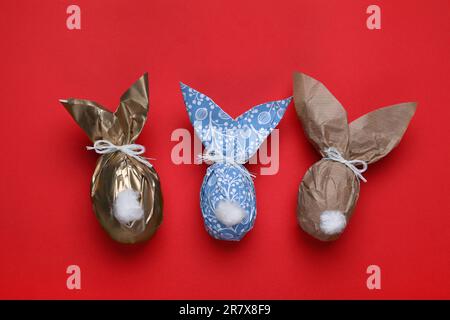 Easter bunnies made of craft paper and eggs on red background, flat lay Stock Photo