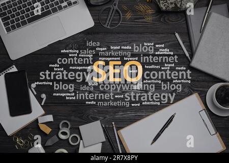 Search engine optimization (SEO). Cloud of words, laptop and stationery on wooden table, flat lay Stock Photo