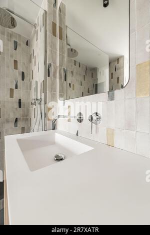 Modern bathroom with frameless mirror, one-piece white porcelain sink, cormed faucets, glass-enclosed shower stall, and accent tile Stock Photo