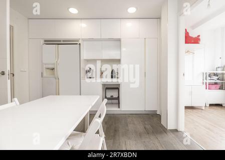 Spacious kitchen with bright white cabinets, light hardwood floors and white built-in appliances Stock Photo