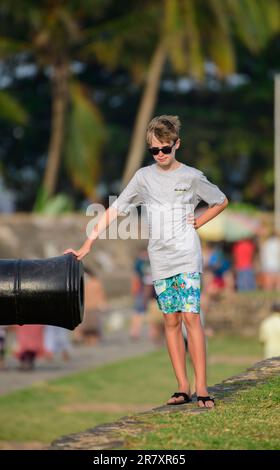 Galle, Sri Lanka - 02 15 2022: A young Caucasian boy with an old canon at Gale Dutch Fort. Stock Photo