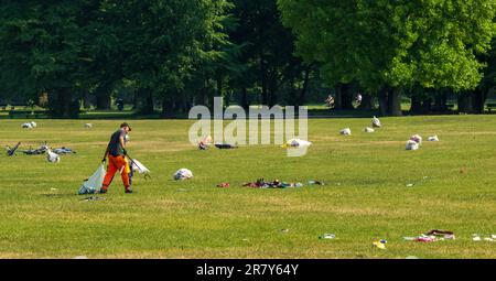 Munich, Germany. 18th June, 2023. An employee of the Stadtwerke cleans up the garbage left behind in large quantities by visitors from the previous day and night on the large lawn in the English Garden. Dozens of beer and wine bottles, broken glass, snack bags and other garbage are lying around in the open space. In the background, the already baked garbage bags are ready for removal. Credit: Peter Kneffel/dpa/Alamy Live News Stock Photo