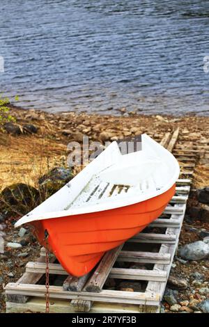 Small orange rowboat moored at riverside in northern Sweden. Stock Photo