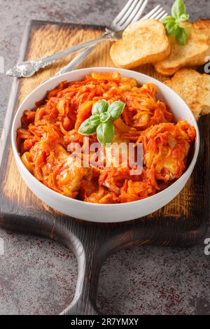 White fish fillet stewed with carrots, onions and celery in tomato sauce served with toast close-up on a wooden board on the table. Vertical Stock Photo