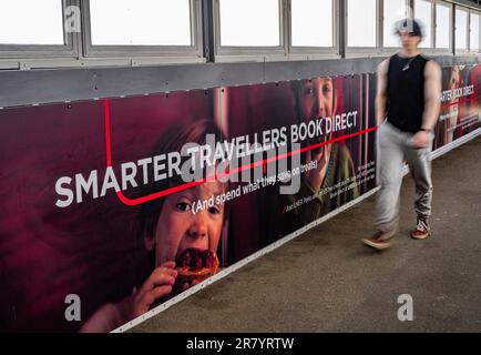 A young man walking past an advertising hoarding for London North Eastern Railway (LNER) for smarter travel and book direct Stock Photo