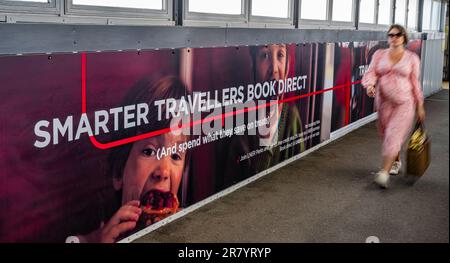 A young woman walking past an advertising hoarding for London North Eastern Railway (LNER) for smarter travel and book direct Stock Photo