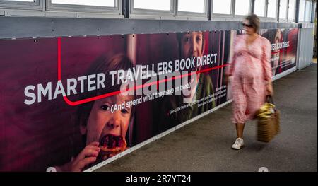 A young woman walking past an advertising hoarding for London North Eastern Railway (LNER) for smarter travel and book direct Stock Photo