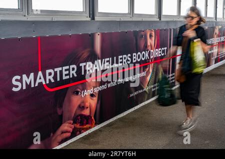 A young woman walking past an advertising hoarding for London North Eastern Railway (LNER) for smarter travel and book direct Stock Photo