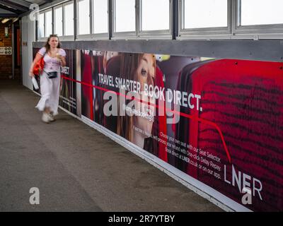 A young woman walking past an advertising hoarding for London North Eastern Railway (LNER) for smarter travel and book direct Stock Photo