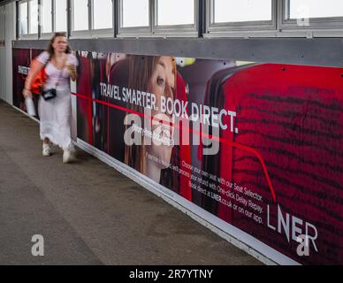 A young woman walking past an advertising hoarding for London North Eastern Railway (LNER) for smarter travel and book direct Stock Photo