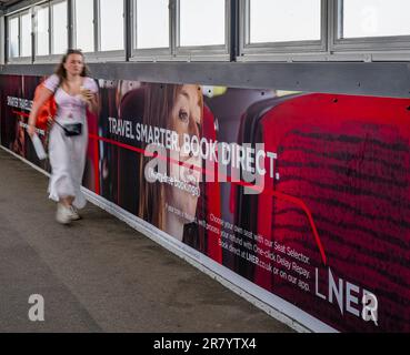 A young woman walking past an advertising hoarding for London North Eastern Railway (LNER) for smarter travel and book direct Stock Photo