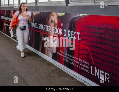 A young woman walking past an advertising hoarding for London North Eastern Railway (LNER) for smarter travel and book direct Stock Photo