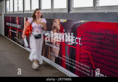 A young woman walking past an advertising hoarding for London North Eastern Railway (LNER) for smarter travel and book direct Stock Photo