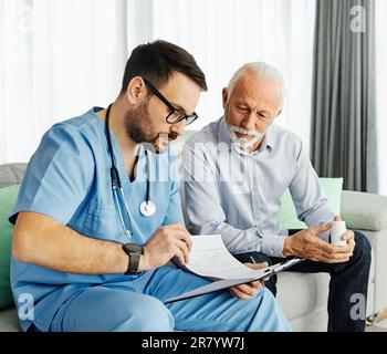 Doctor or nurse caregiver showing a prescrption or documents and holding drug bottle to senior man at home or nursing home Stock Photo