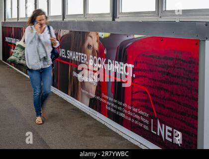 Woman on mobile phone walking past an advertising hoarding for London North Eastern Railway (LNER) for smarter travel and book direct Stock Photo